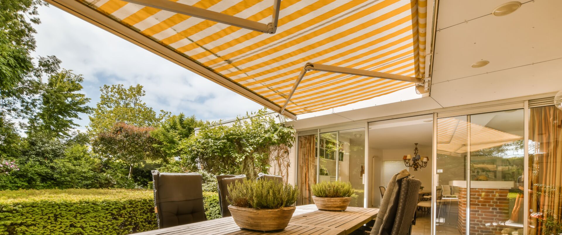 Eine Terrasse mit einer ausgefahrenen Markise, Möbeln und Pflanzen.